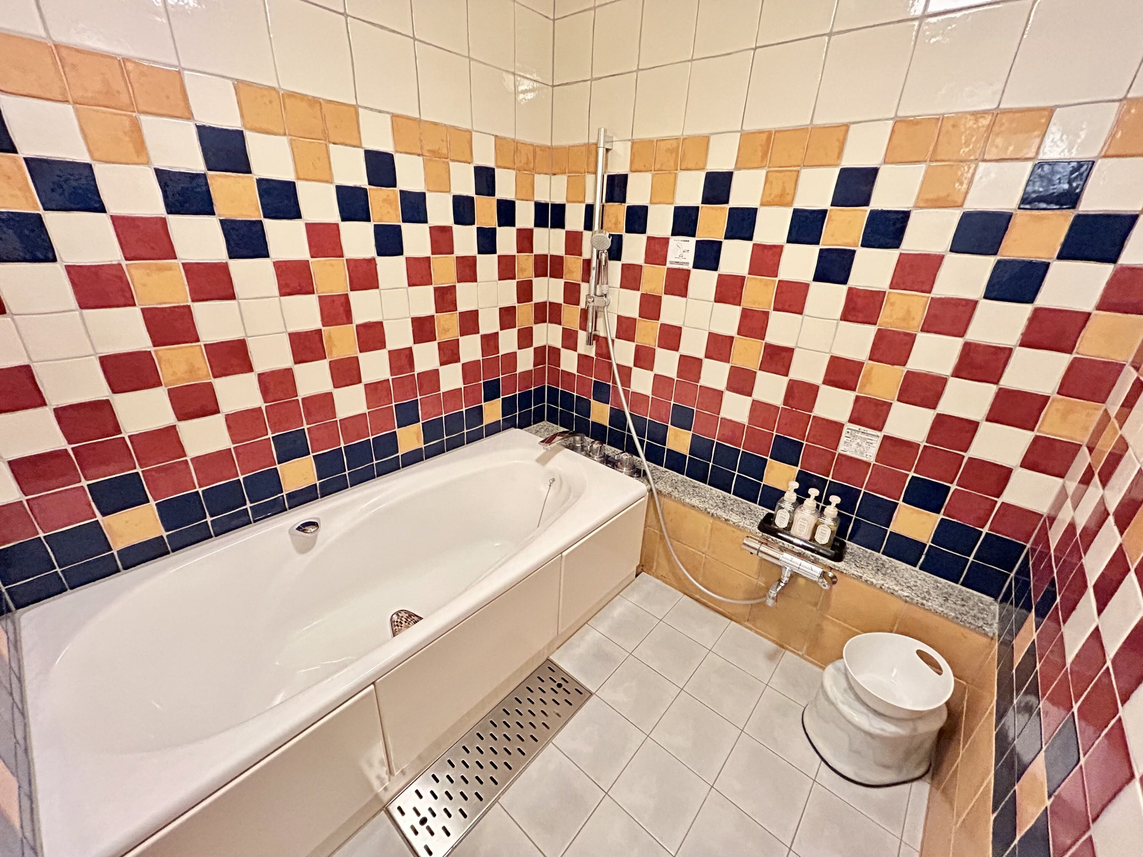 A bathroom with a checkered tile wall, a bathtub, a toilet, and a shower area.