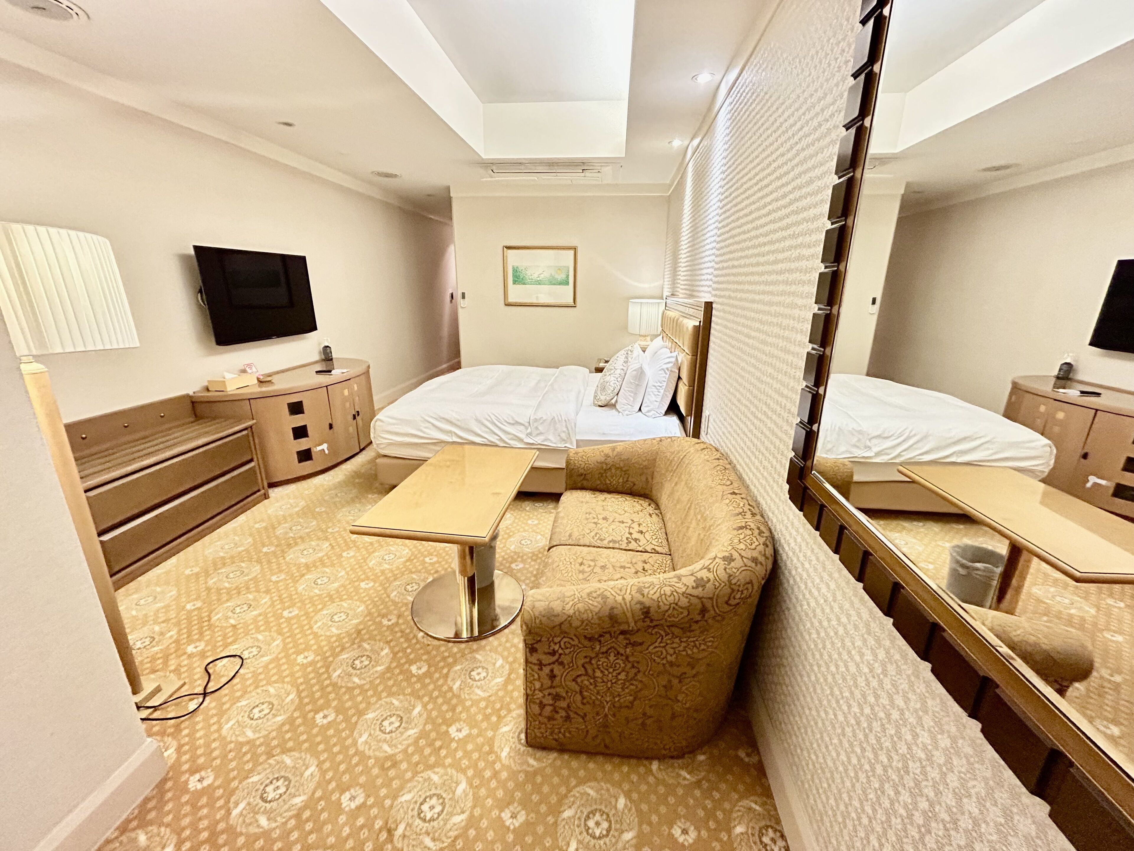 Una habitación de hotel con cama, sofá, escritorio, televisor y espejo.