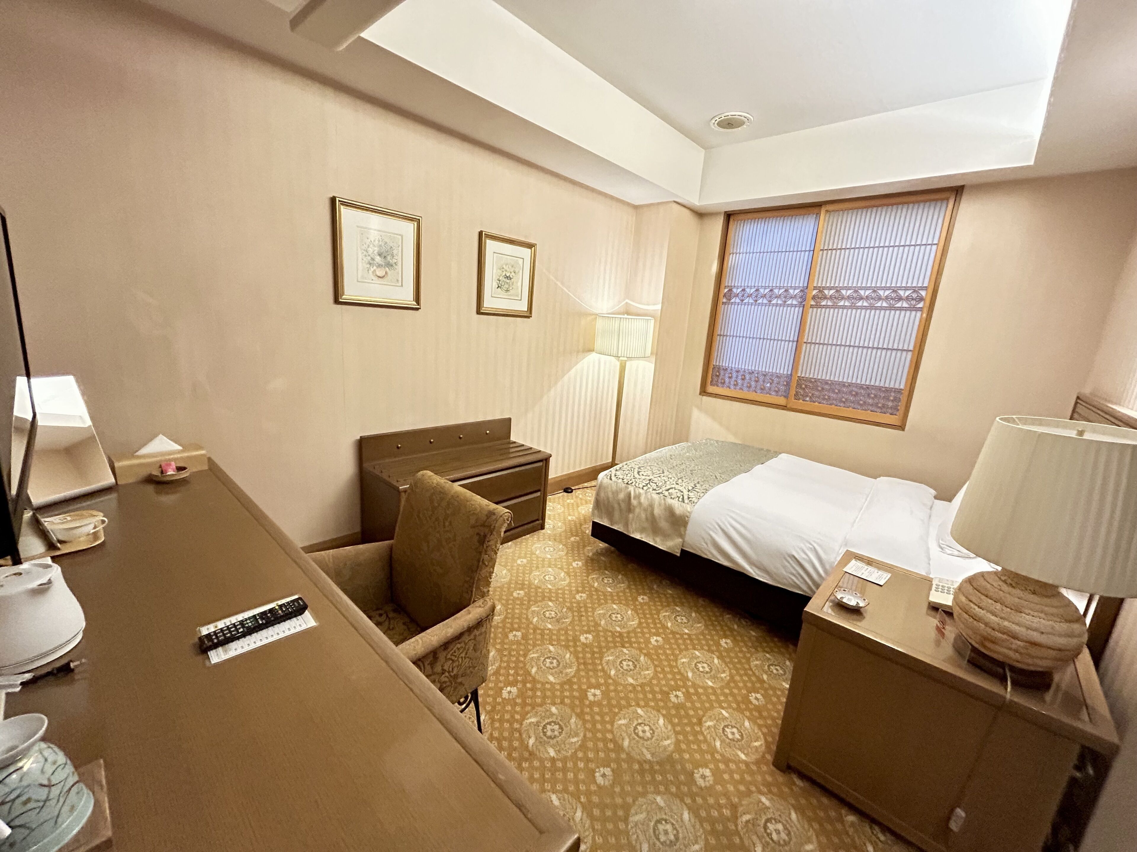 A hotel room with a bed, desk, chair, and a window with blinds.