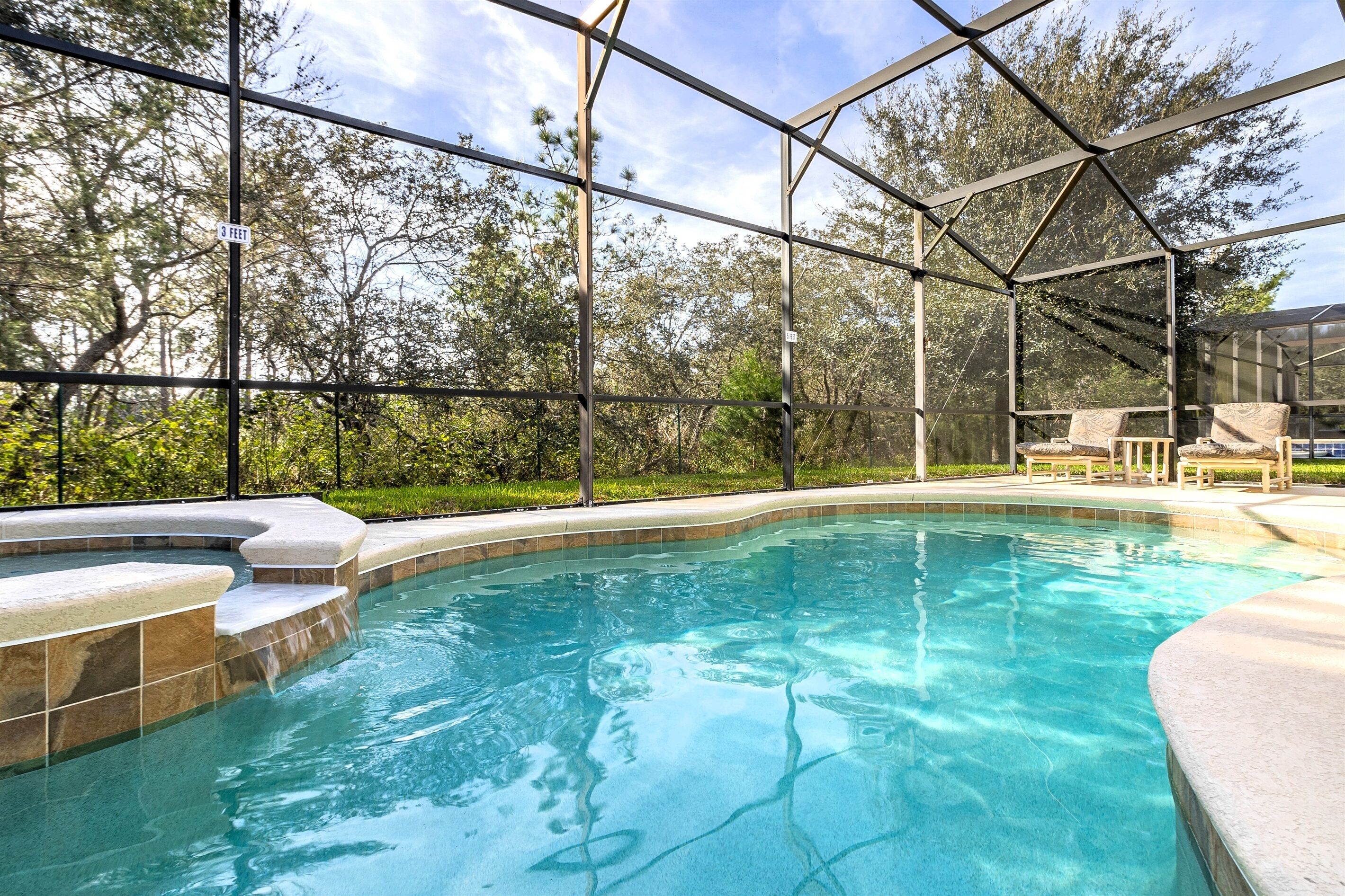 A swimming pool with a glass enclosure, surrounded by a landscaped area and trees.