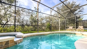 A swimming pool with a glass enclosure, surrounded by a landscaped area and trees. - The Mandalori-Inn - South Pool, Conservation View! (Kissimmee)