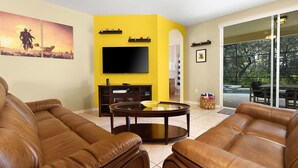 A living room with brown leather sofas, a glass coffee table, a flat-screen TV, and a yellow accent wall. - The Mandalori-Inn - South Pool, Conservation View! (Kissimmee)