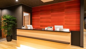 A reception desk with a modern design, a potted plant, and a red wall in the background. - Sekaiisannokakureyado Kajitsunomori (Ichinoseki)