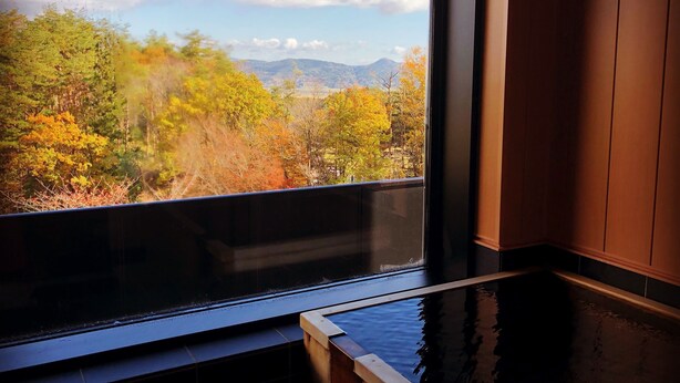 A room with a large window offering a view of autumn foliage and mountains. - Sekaiisannokakureyado Kajitsunomori (Ichinoseki)