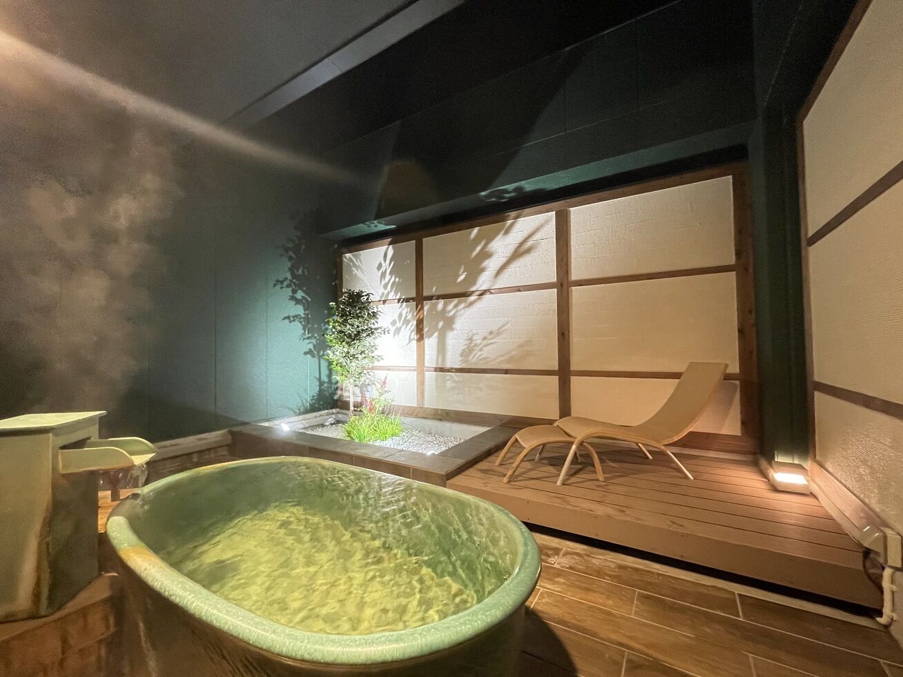 A traditional Japanese onsen with a stone hot tub, a small garden, and a wooden deck.