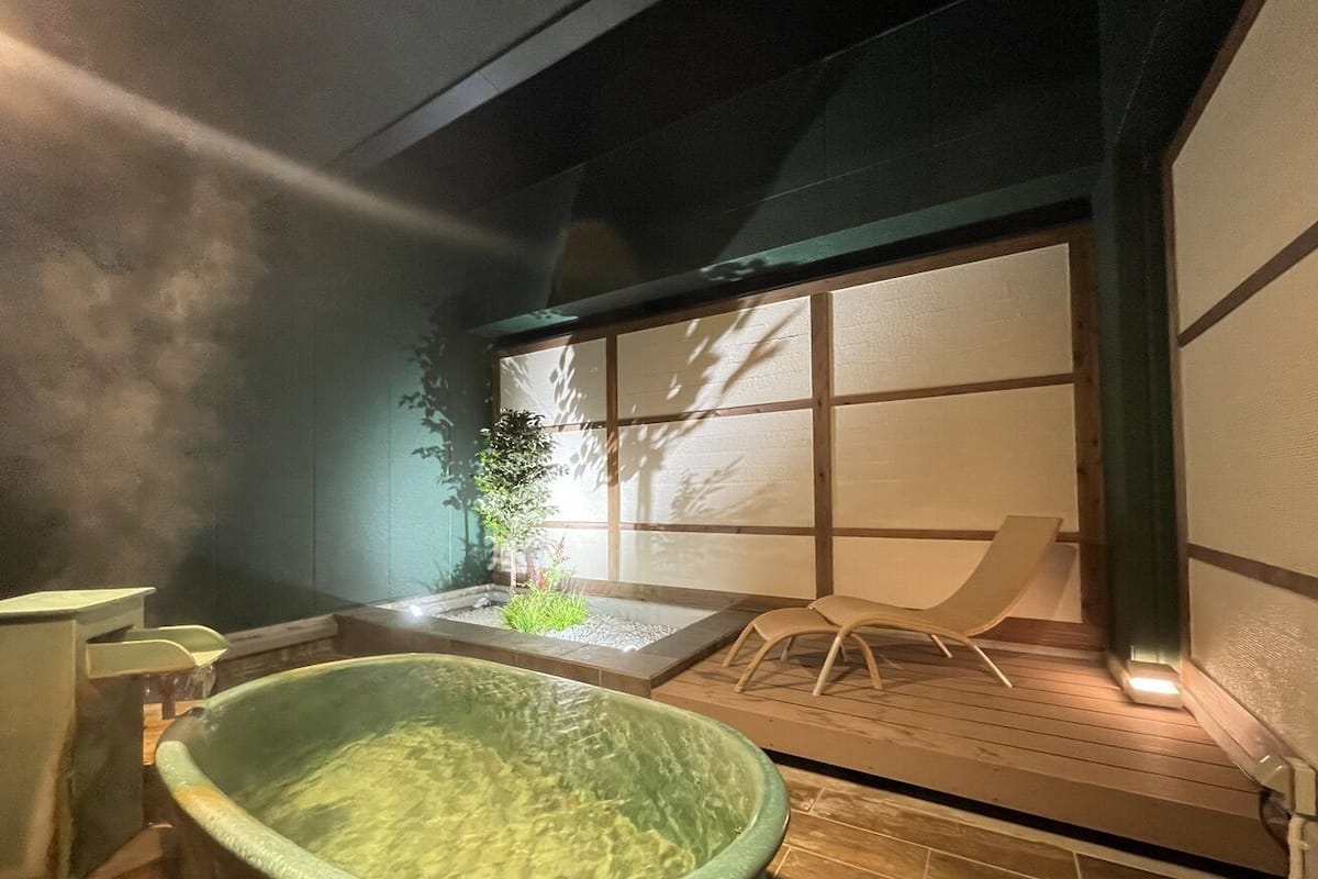 Ein traditionelles japanisches Onsen mit einem Steingrot-Bad, einem kleinen Garten und einer Holzterrasse.