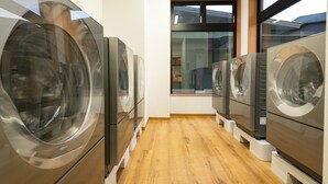 A laundry facility with multiple washing machines arranged in a row, wooden flooring, and a window providing natural light. - Sekaiisannokakureyado Kajitsunomori (Ichinoseki)