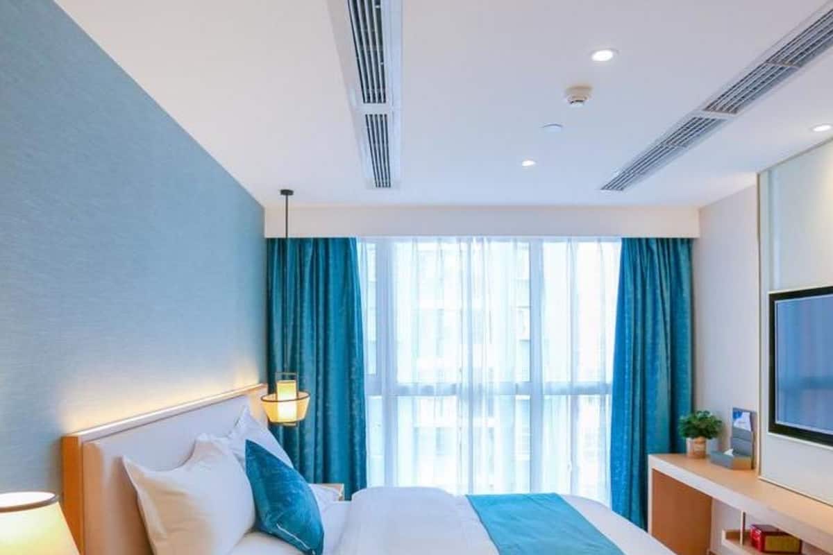 A modern hotel room with a bed, a TV, a nightstand, and a window with curtains.