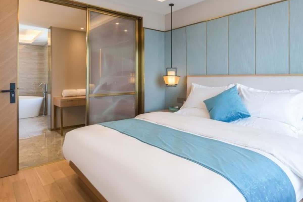 A modern hotel room with a large bed, a nightstand, a wall-mounted lamp, and a sliding door leading to a bathroom.