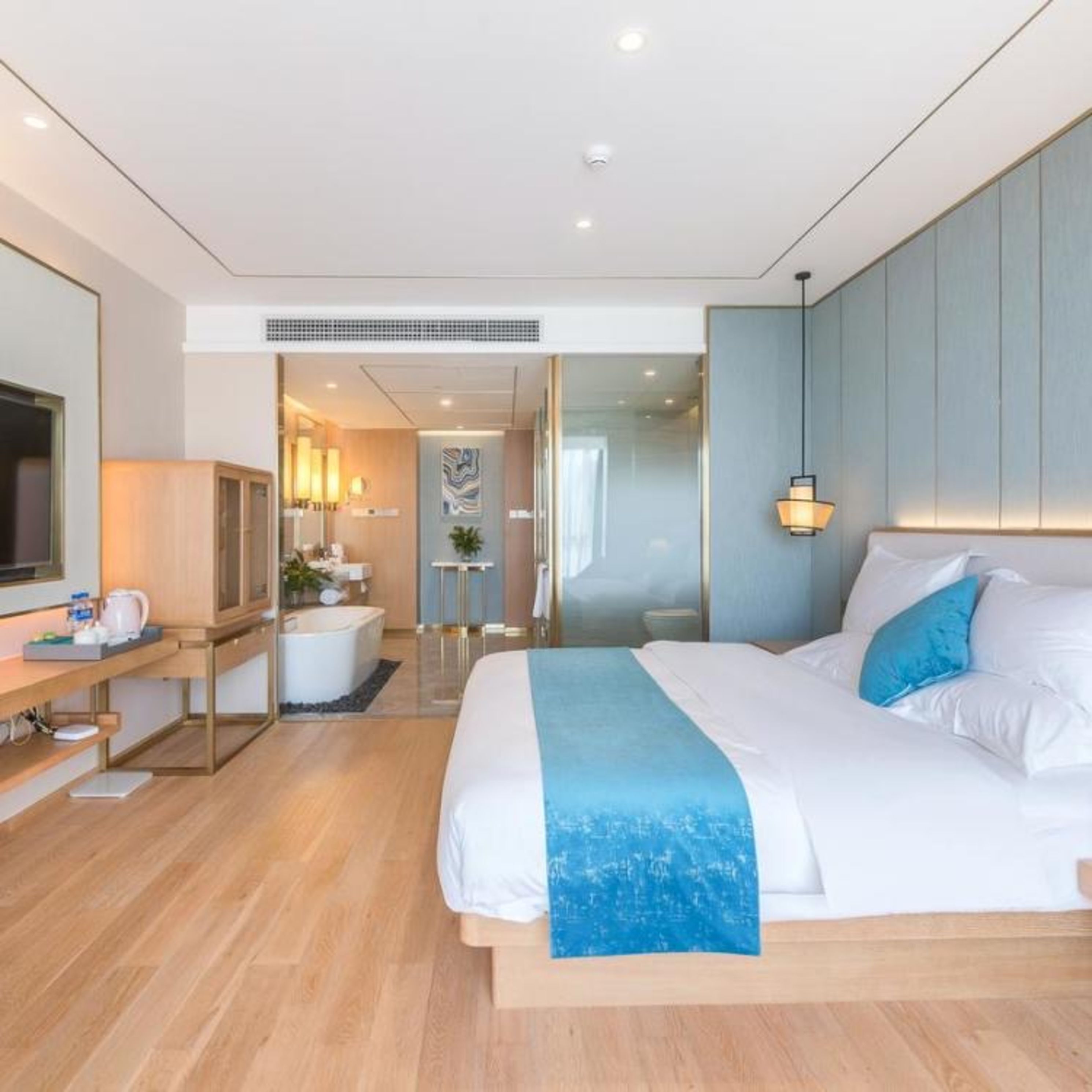 A modern hotel room with a large bed, a desk, a TV, and a bathroom visible through an open door.