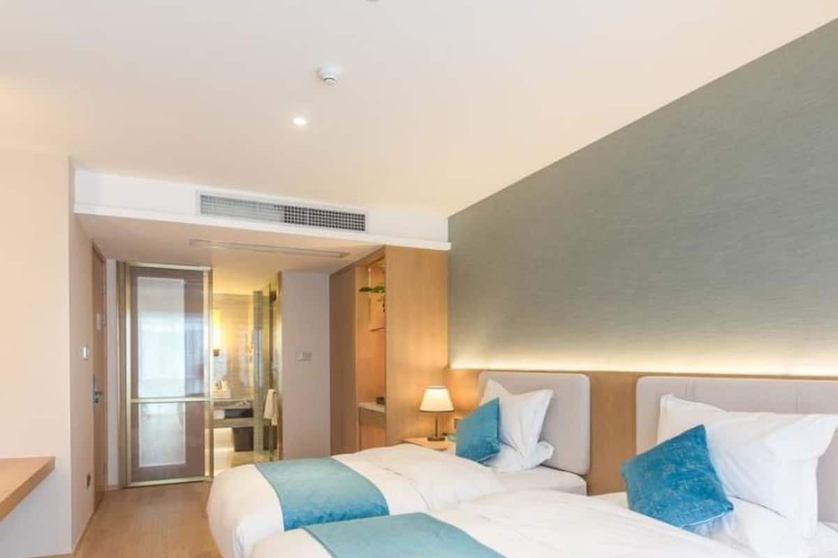 A hotel room with two beds, a bathroom, and a hallway leading to another room.