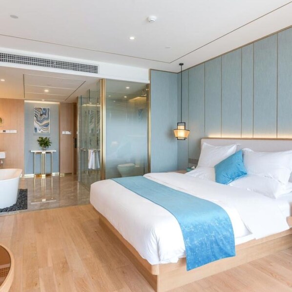 Une chambre d’hôtel moderne avec un grand lit, une table de chevet, une lampe fixée au mur et une cabine de douche en verre.