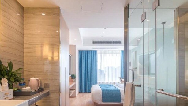 Moderni hotellihuone, jossa on lasiseinäinen suihkutila, suuri sänky, jossa on sininen tehosteväri, ja kylpyhuone, jonka lattia on marmoria.