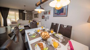 Ein Essbereich mit einem Tisch, gedeckt für ein Frühstück, darunter Croissants, Orangensaft und ein Korb mit Brot.