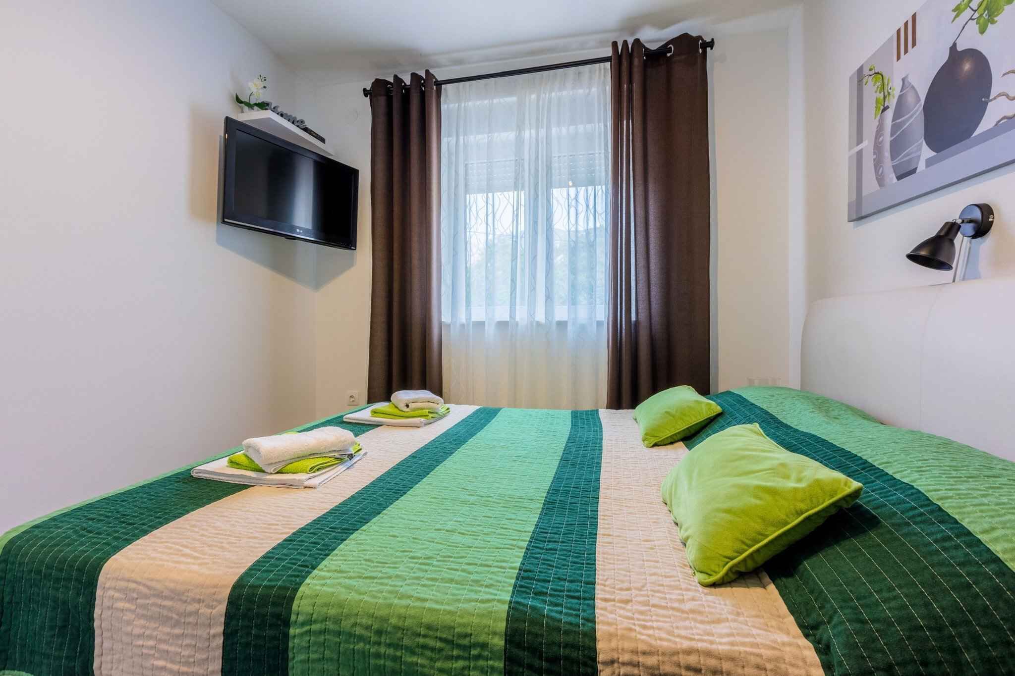 Habitación de hotel con cama, televisión de pantalla plana, ventana con cortinas y un cuadro en la pared.