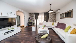 Ein modernes Wohnzimmer mit einem Flachbildfernseher, weißen Sofas, einem Couchtisch und einem Kamin aus Stein.