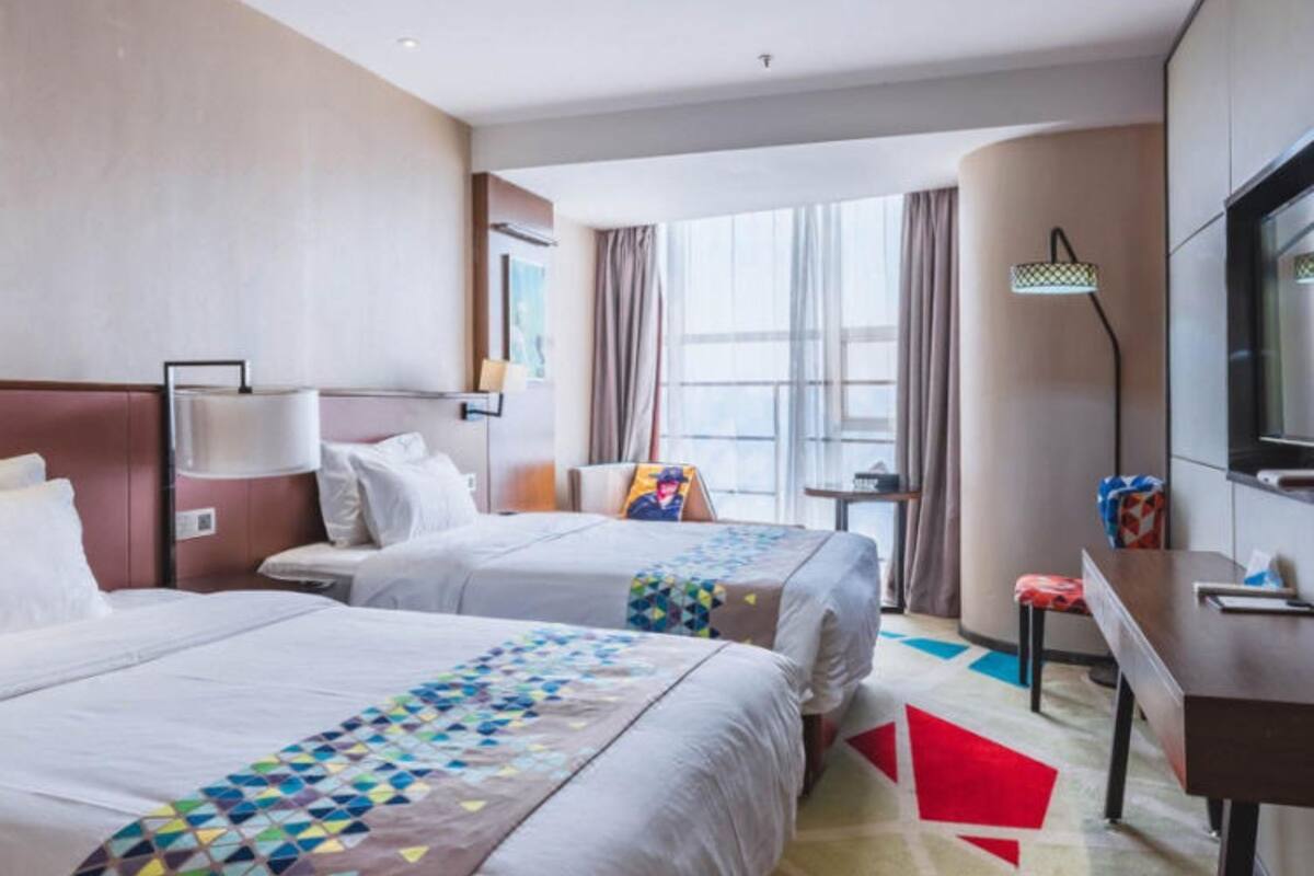 A hotel room with two beds, a desk, a TV, and a window with curtains.