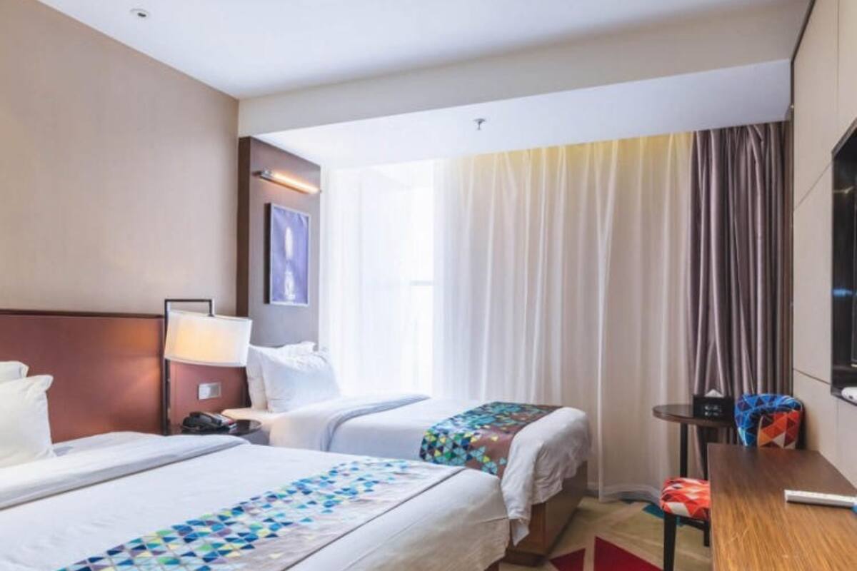 A hotel room with two beds, a desk, a chair, a TV, and a window with curtains.