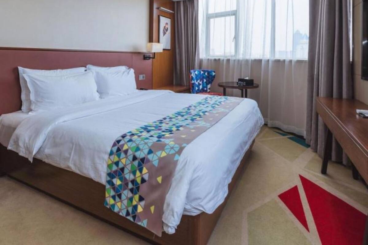 A hotel room with a large bed, a desk, a chair, a TV, and a window with curtains.