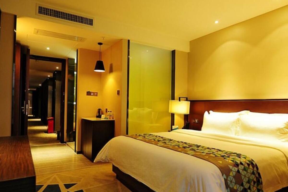 A hotel room with a large bed, a bedside table, a nightstand, a lamp, and a door leading to another room.