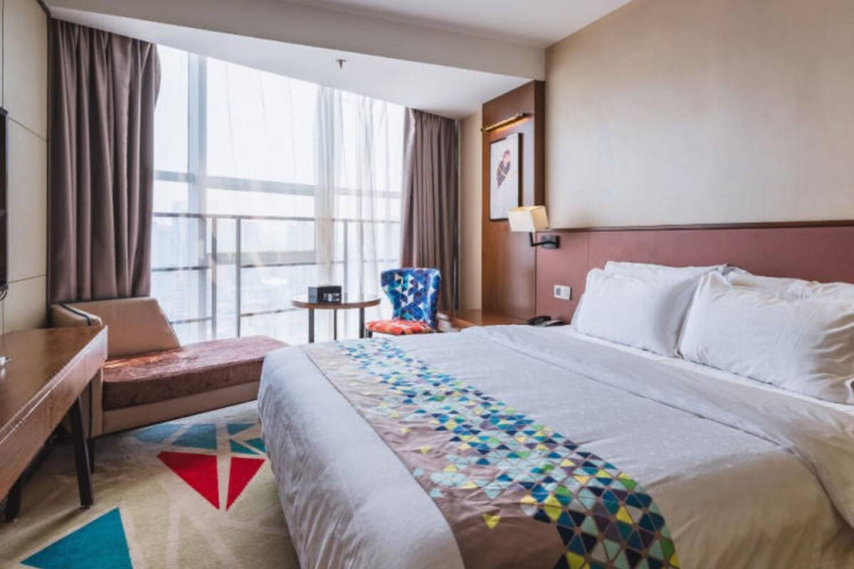 A hotel room with a large bed, a desk, a chair, and a window with curtains.