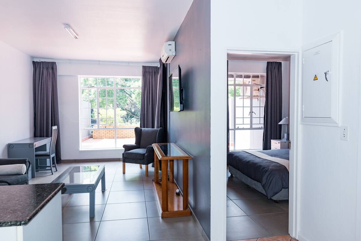 A modern hotel room with a dining area, a bed, and a TV mounted on the wall.