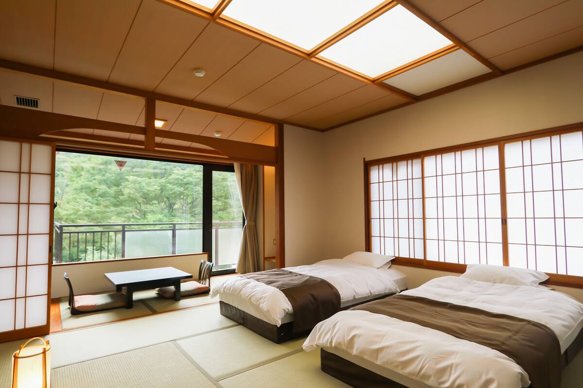 A traditional Japanese-style bedroom with tatami flooring, a sliding door, and a view of greenery outside.