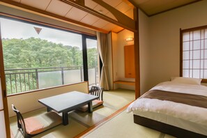 Una habitación con suelo de tatami, una cama, una mesa y vistas a un bosque a través de un ventanal grande.
