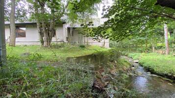 A natural outdoor area with a stream, trees, and a building in the background.