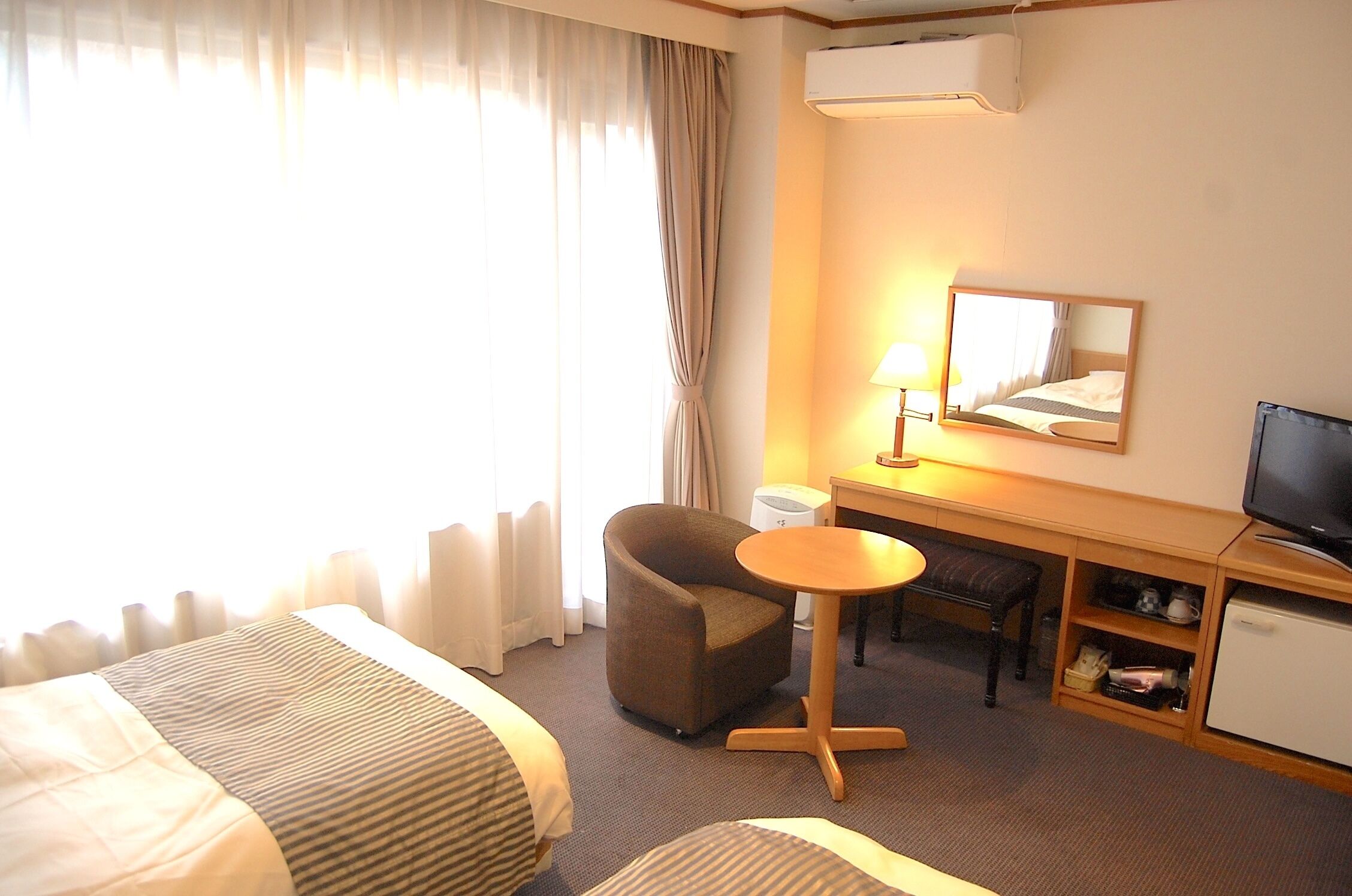 A hotel room with a bed, a desk with a chair, a television, and a small refrigerator.