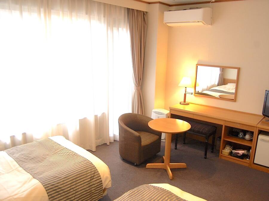 A hotel room with a bed, a desk with a chair, a television, and a small refrigerator.