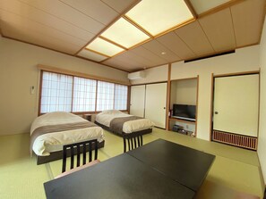 Habitación con dos camas, una mesa, un televisor y puertas correderas.