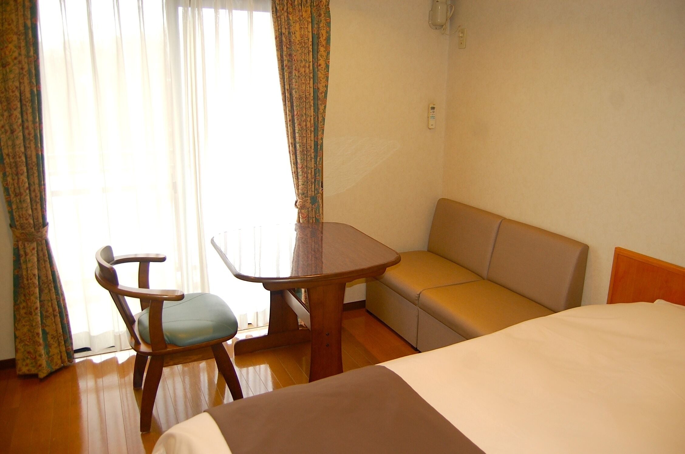 A hotel room with a bed, a wooden table, a chair, a sofa, and a window with curtains.