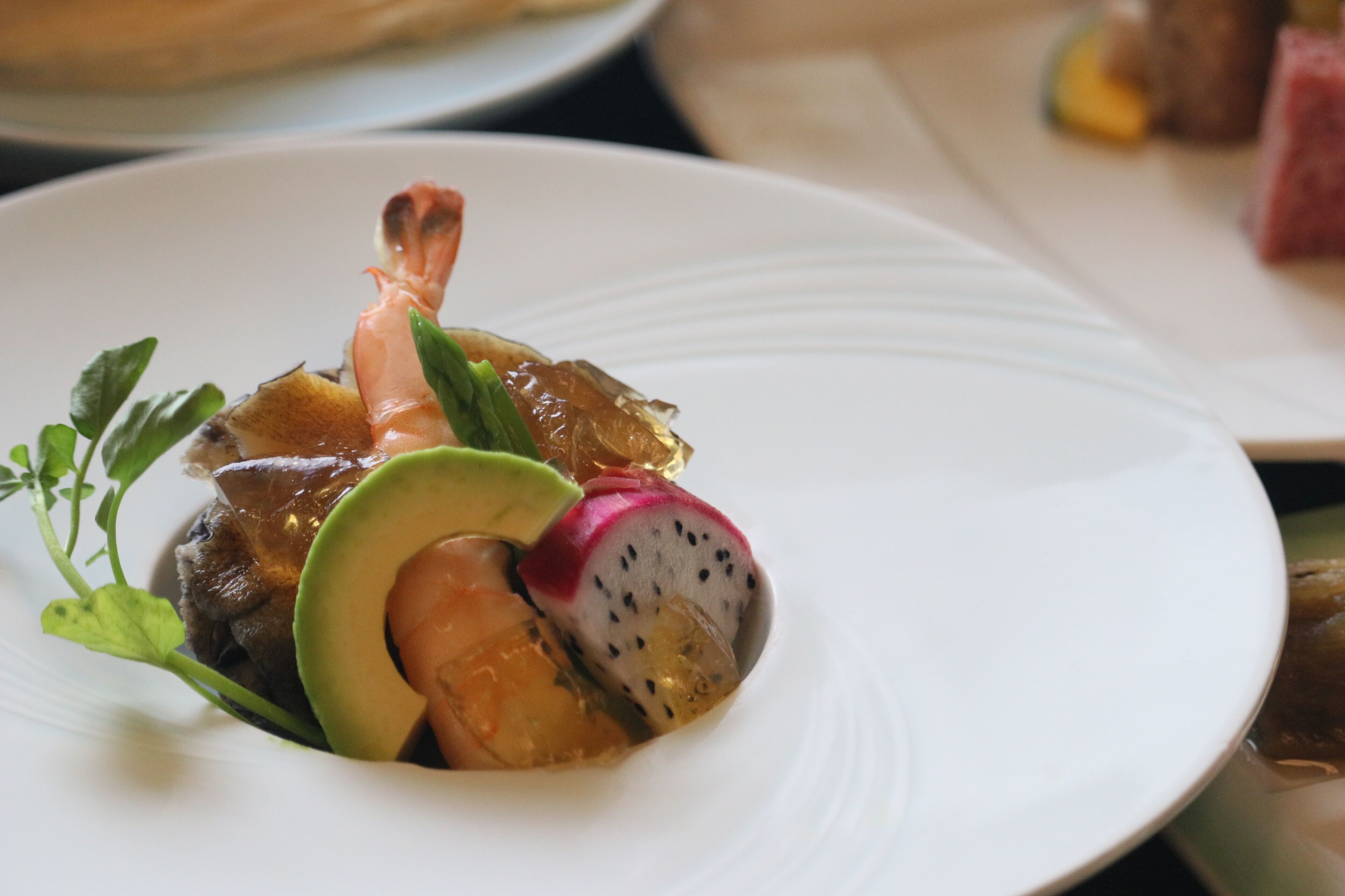 A plate with a dish consisting of a shrimp, avocado, and a slice of radish.