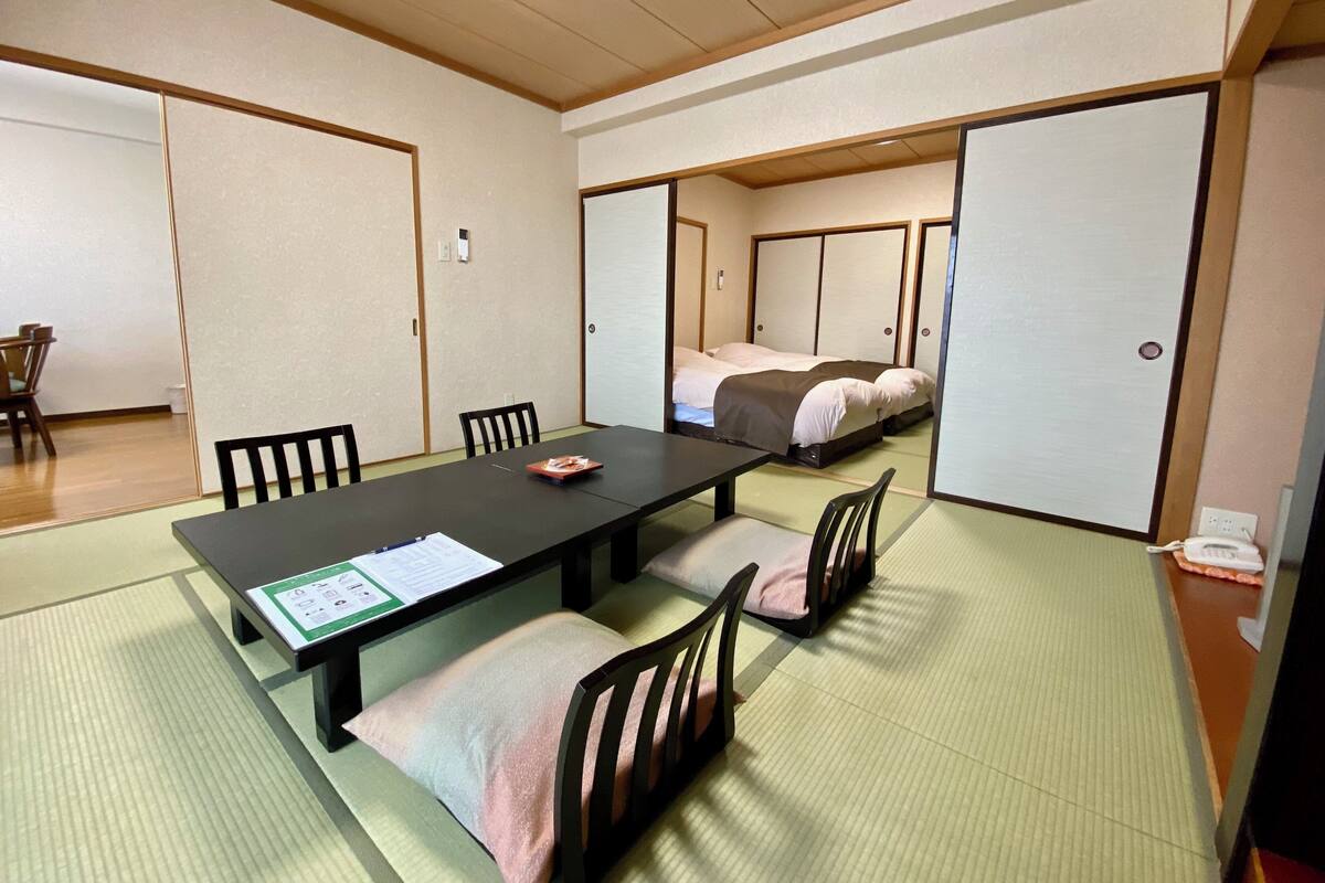 A traditional Japanese room with tatami flooring, a low table with a menu, and a bed with futon-style bedding.
