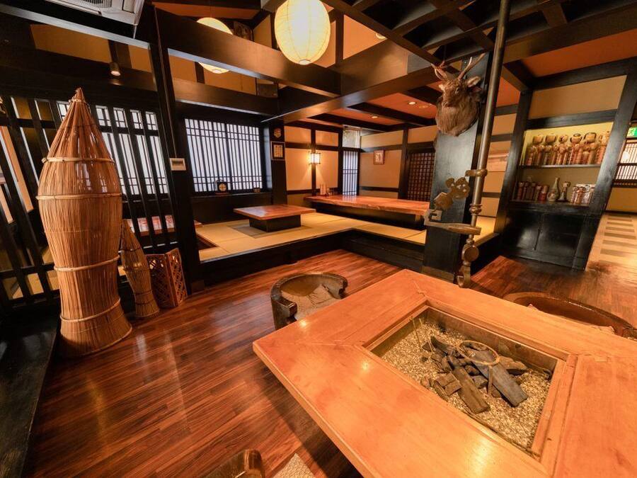 Una habitación tradicional japonesa con suelo de tatami, un celosía shoji, una mesa de madera con un brasero y una decoración de cabeza de ciervo.