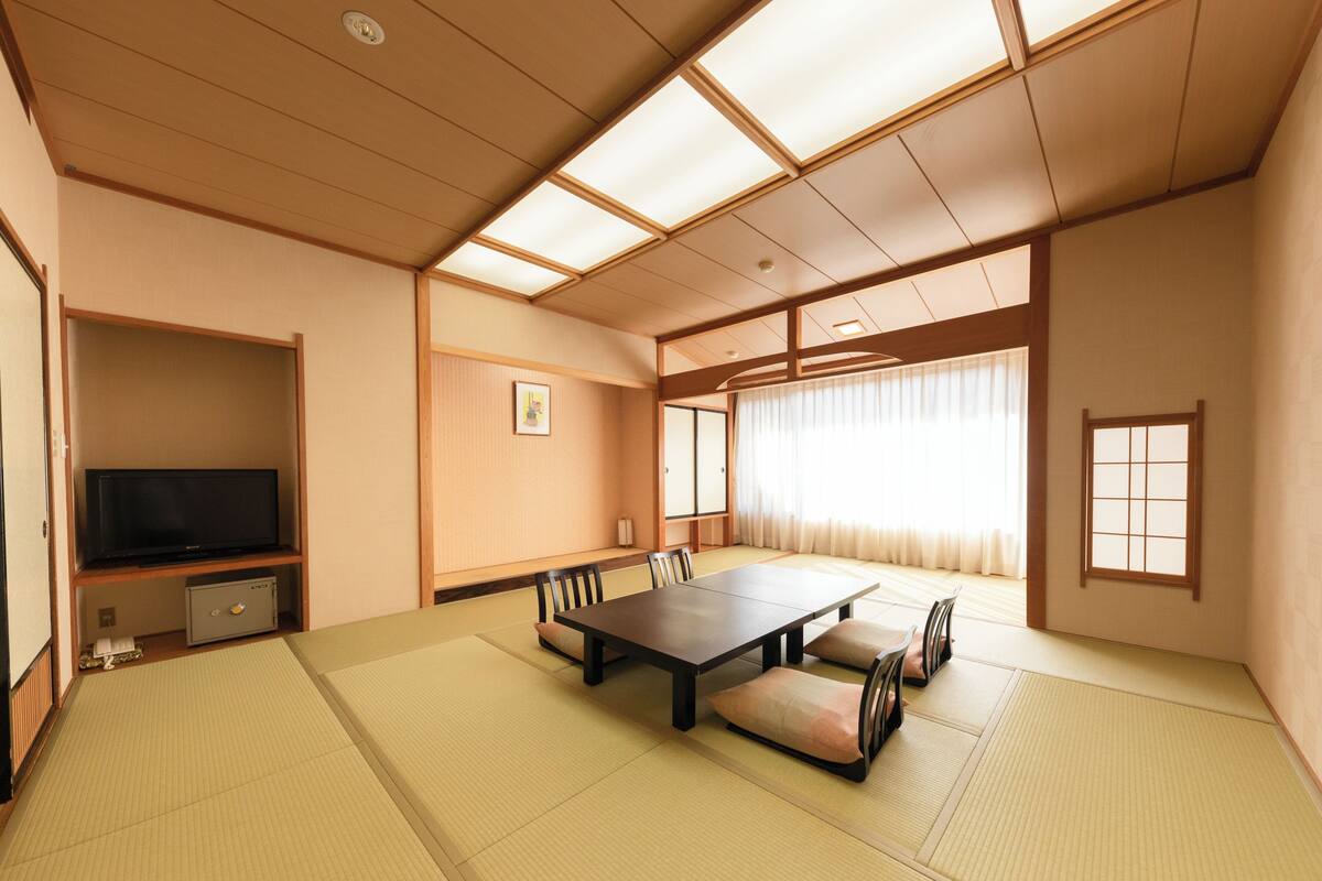 A traditional Japanese-style room with tatami flooring, a low table, and a television on a shelf.