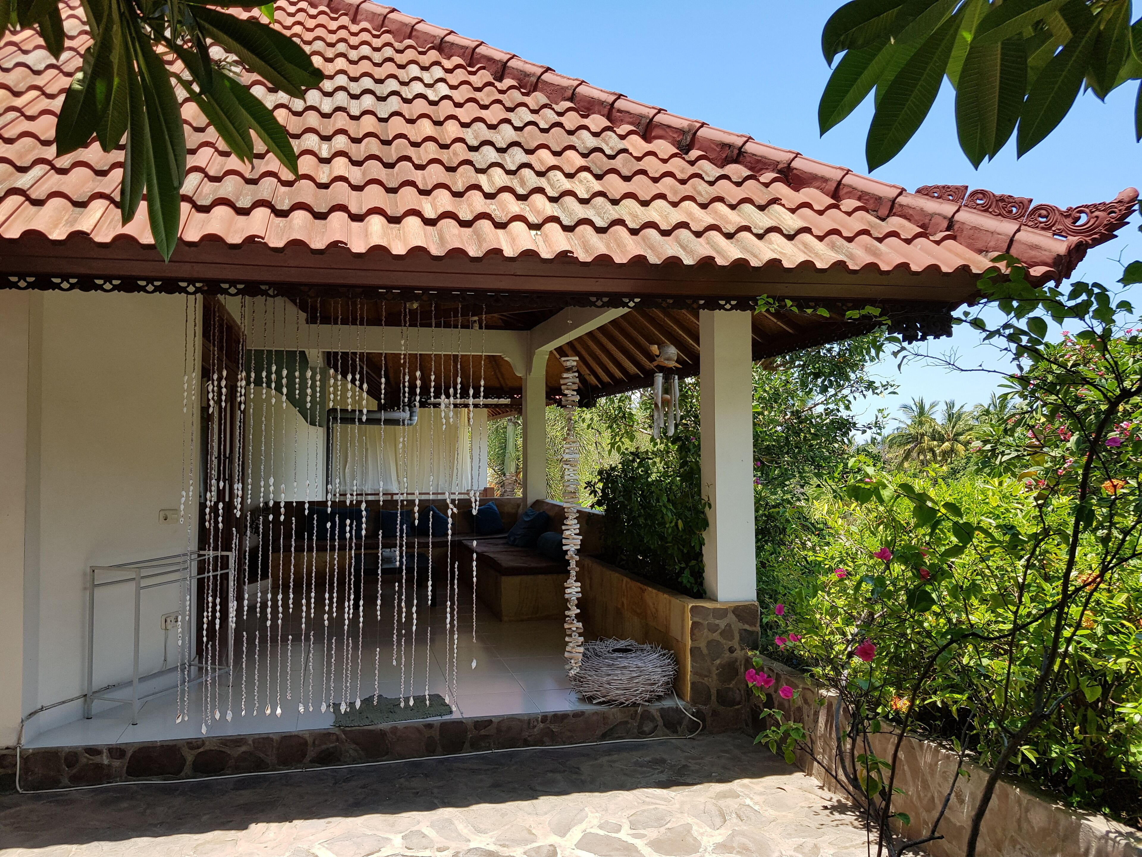 A covered outdoor seating area with a tiled roof, stone steps, and hanging decorative elements.