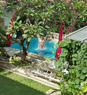 Una piscina rodeada de vegetación exuberante y sombrillas rojas.