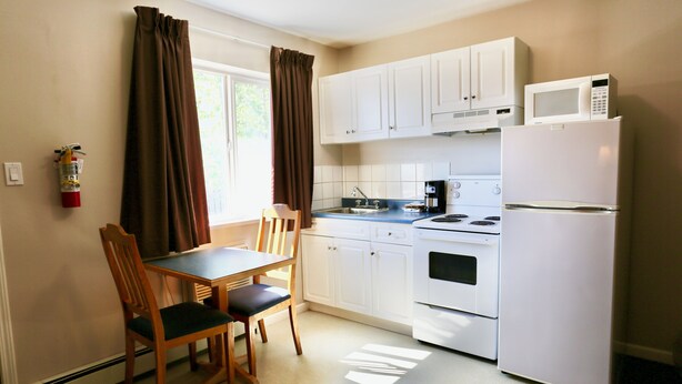 A compact kitchen with white cabinets, a microwave, a stove, and a table with chairs.