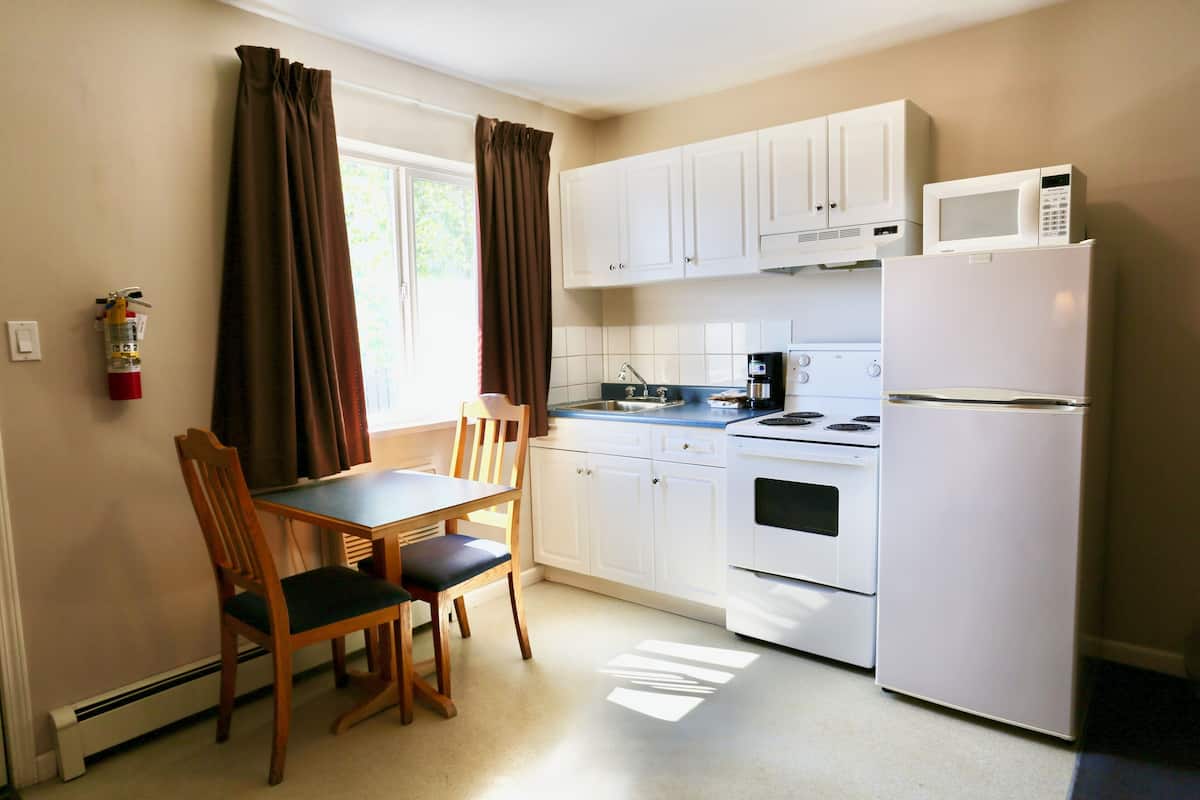 A compact kitchen with white cabinets, a microwave, a stove, and a table with chairs.