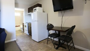 A compact kitchen with a refrigerator, microwave, and oven. A flat-screen TV is mounted on the wall.