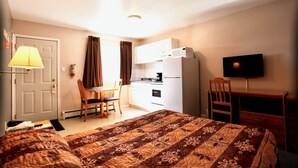 A hotel room with a bed, a desk, a chair, a television, and a kitchenette.