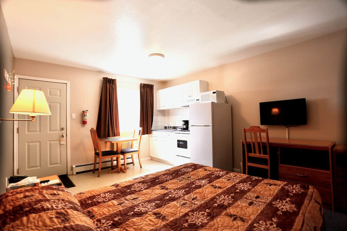 A hotel room with a bed, a desk, a chair, a television, and a kitchenette.