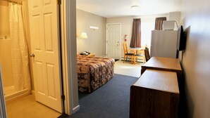 A hotel room with a bed, a desk, a chair, a laptop, and a television.