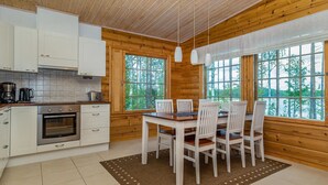 Interior de una cabaña de madera con cocina, comedor y ventanas amplias.