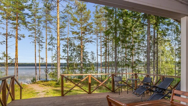Una terraza de madera con una mesa y sillas, con vista a un lago rodeado de árboles y un cielo despejado.