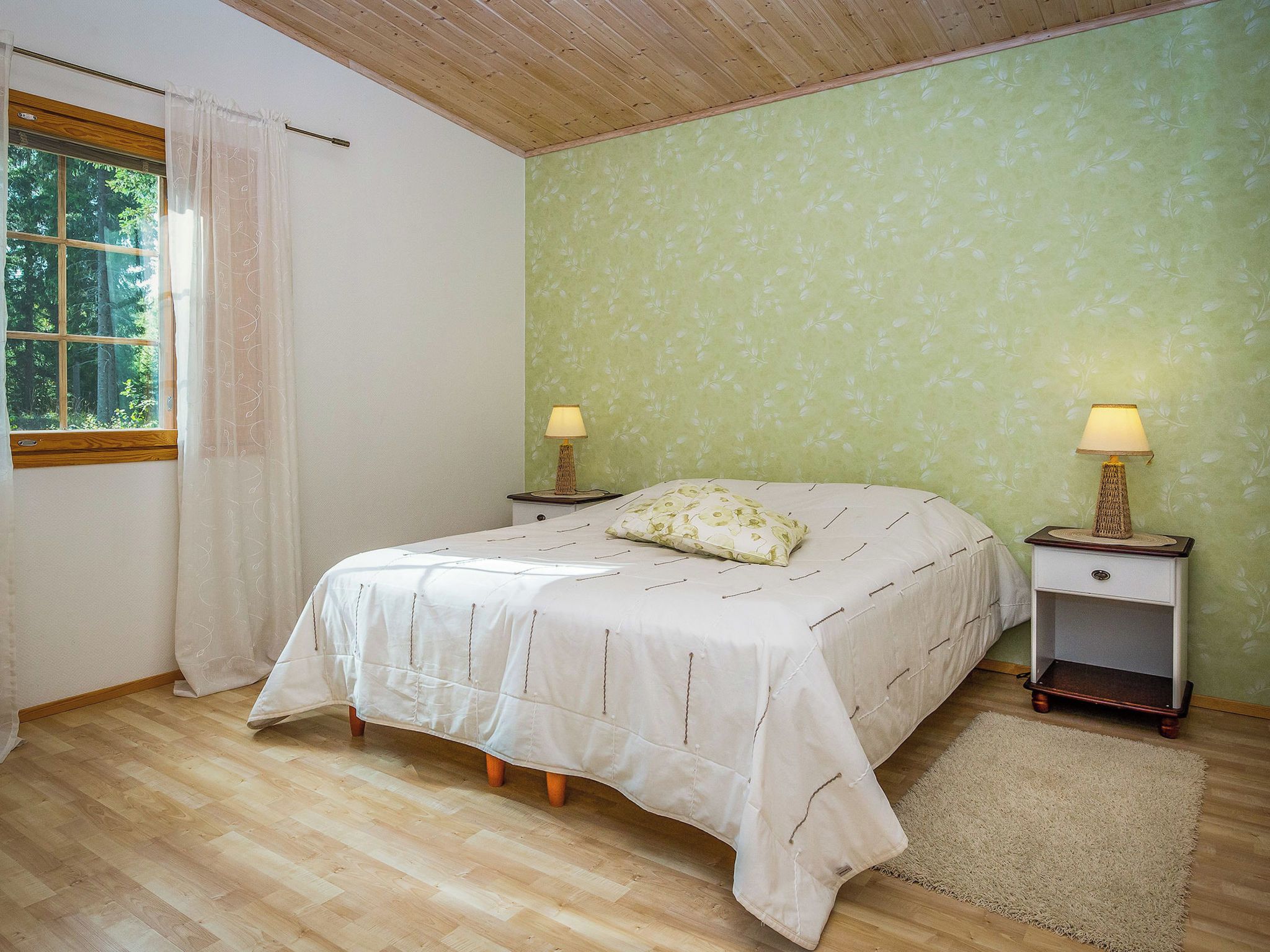 Una camera da letto con un letto, due comodini con lampade, una finestra con tende e un muro decorato.