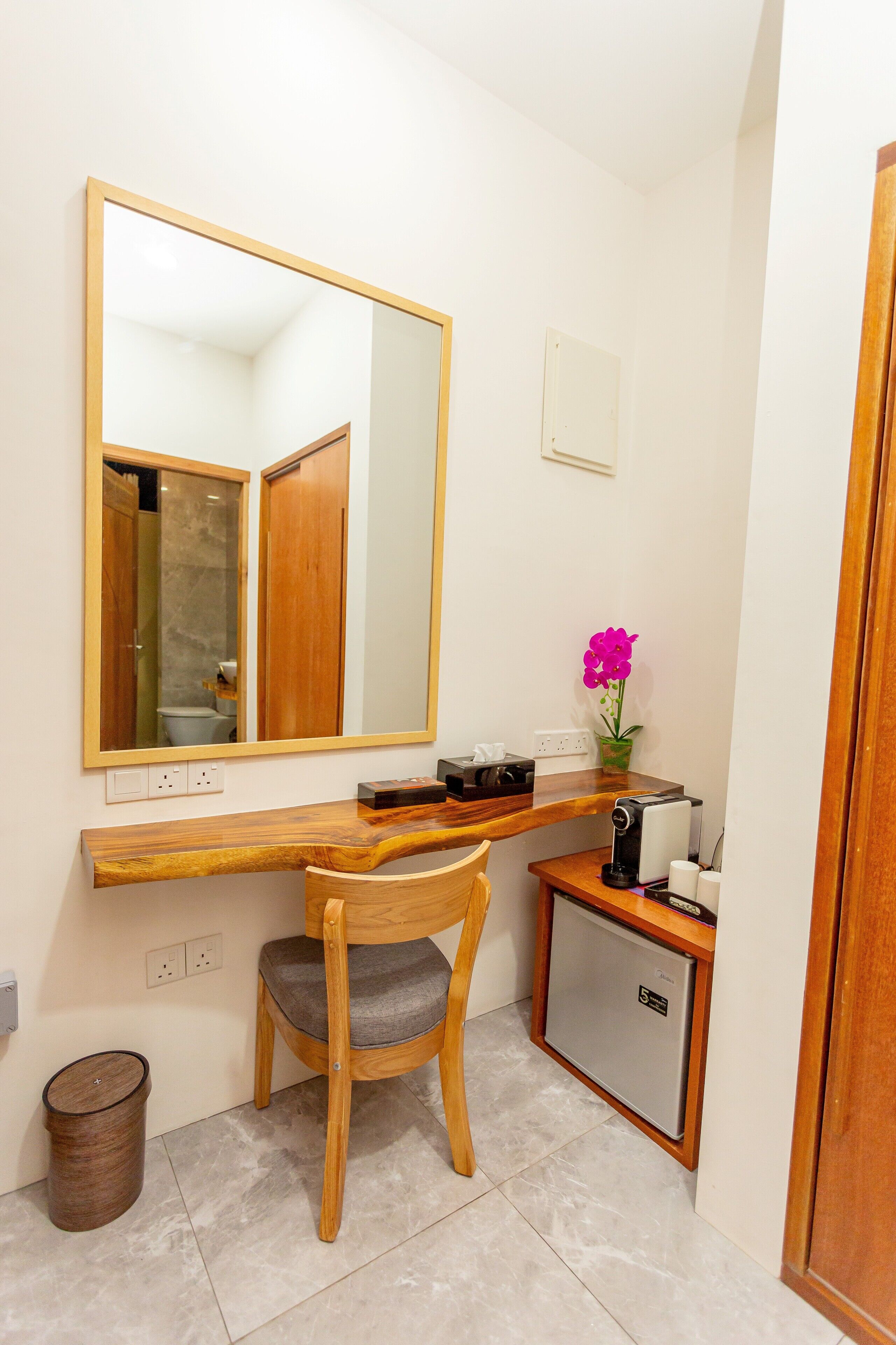 A compact bathroom with a wooden vanity, a small refrigerator, a chair, and a mirror.