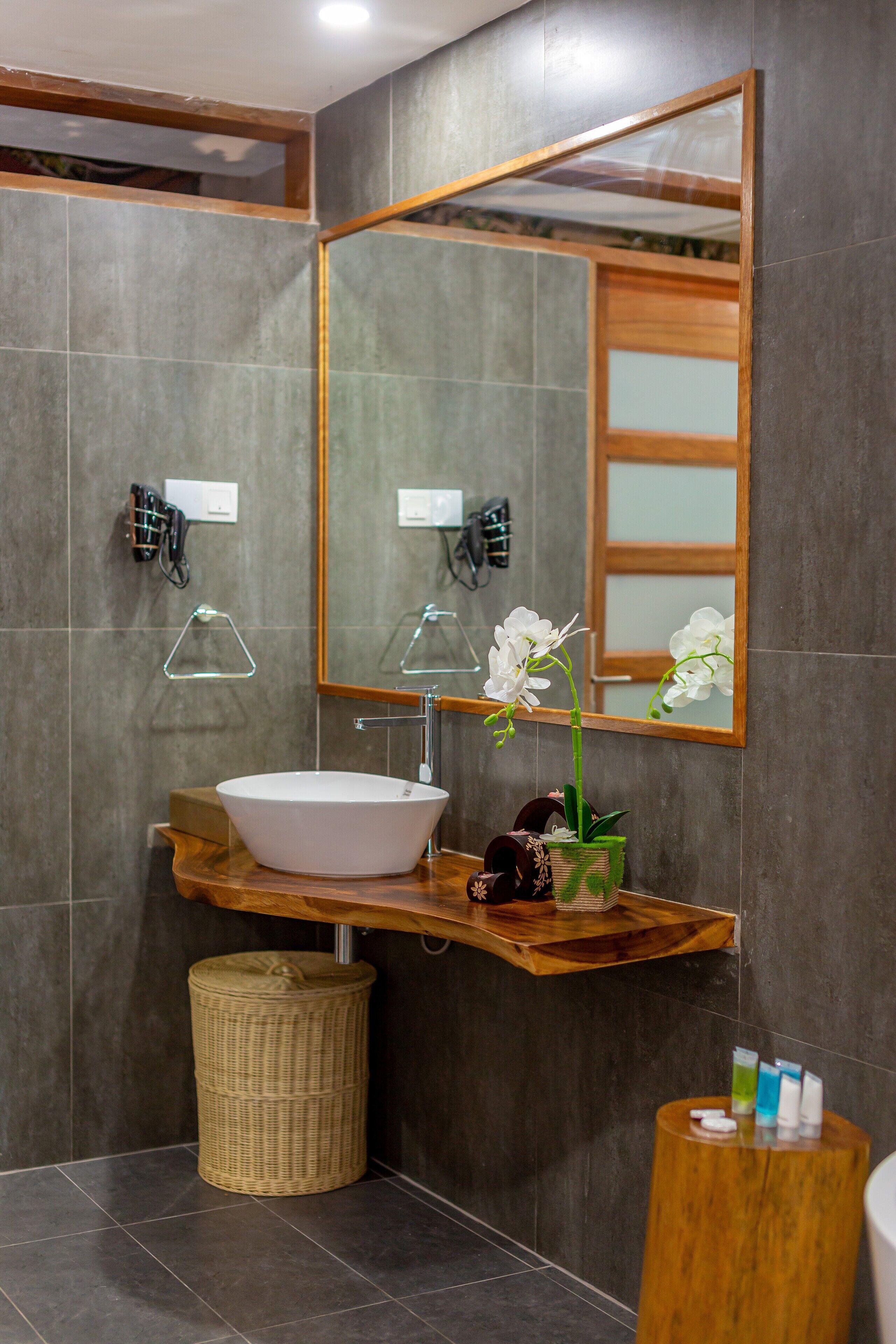 Une salle de bain moderne avec un grand miroir, un meuble-lavabo en bois, un lavabo blanc et un panier en osier.